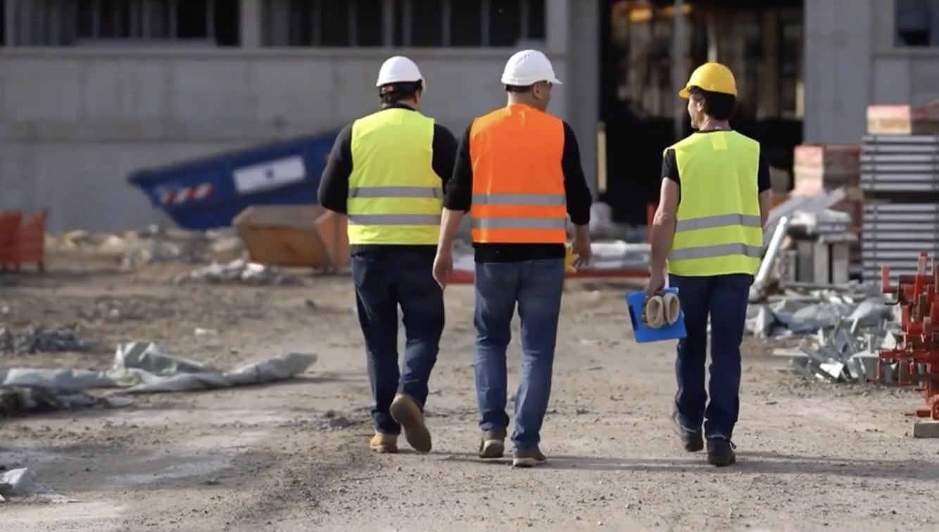 Three construction workers in safety vests walking across a job site